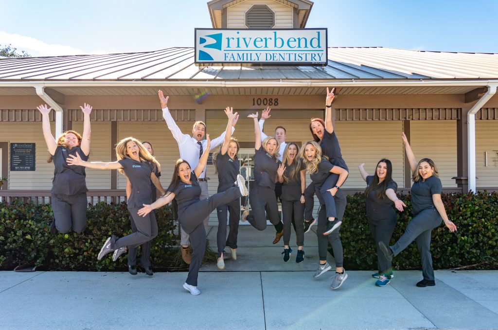 Riverbend Family Dentistry team jumping outdoors in front of dental office building.