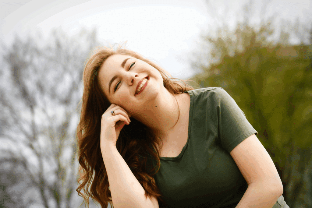 Happy woman in green shirt smiling outdoors, showcasing cosmetic dental results.